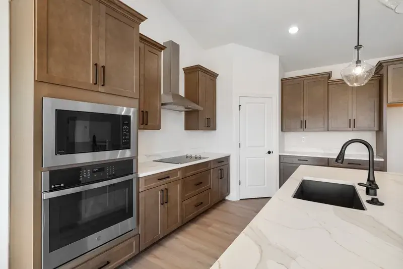 empty kitchen in a new home shows brown cabinets with stainless fixtures and kitchen island
